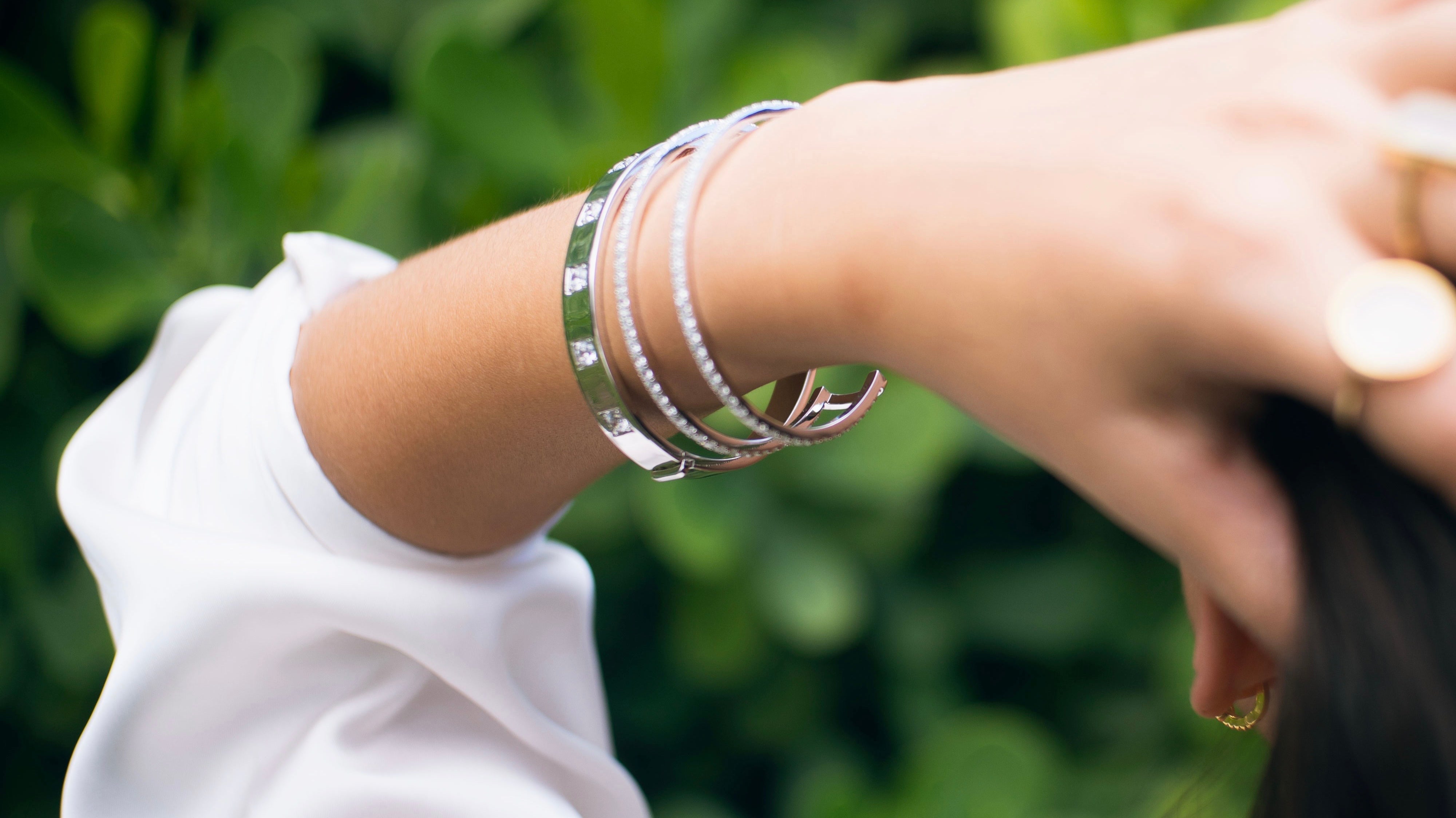 model is wearing two white gold bangles: one is a two-row pave cuff; the other is a six-stone bangle with white CZs