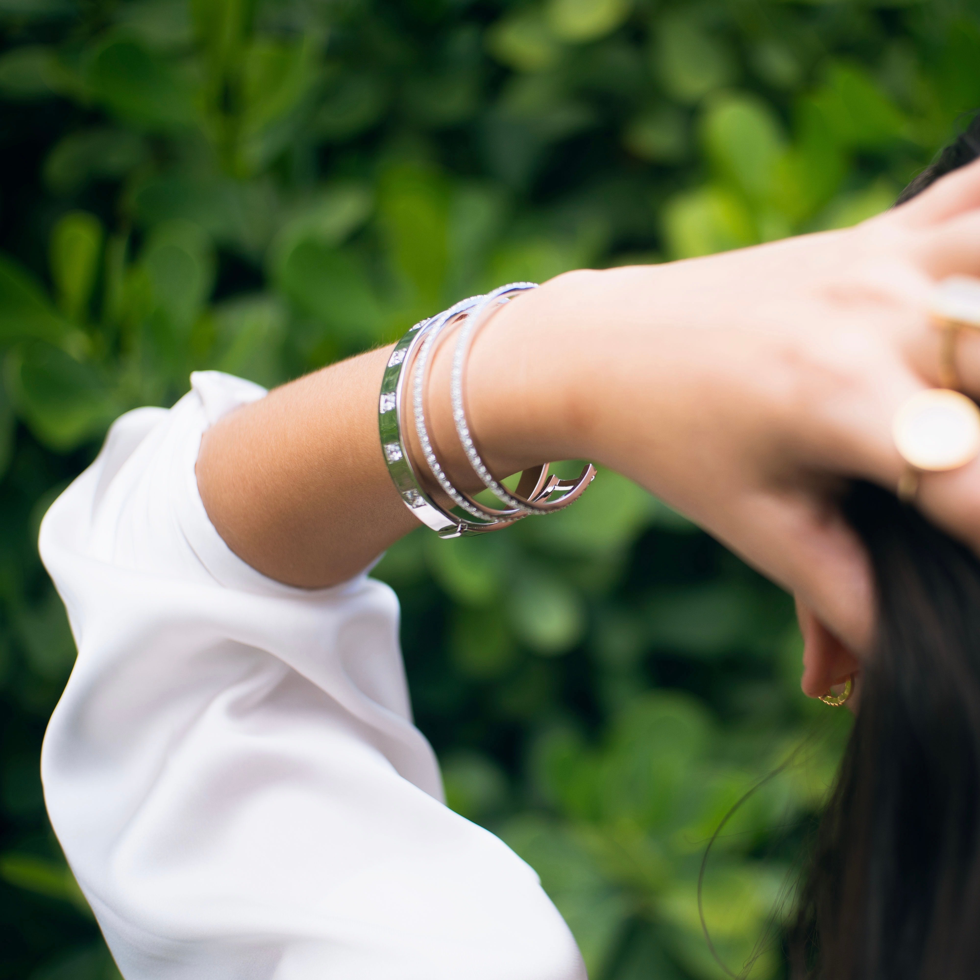 model is wearing two white gold bangles: one is a two-row pave cuff; the other is a six-stone bangle with white CZs